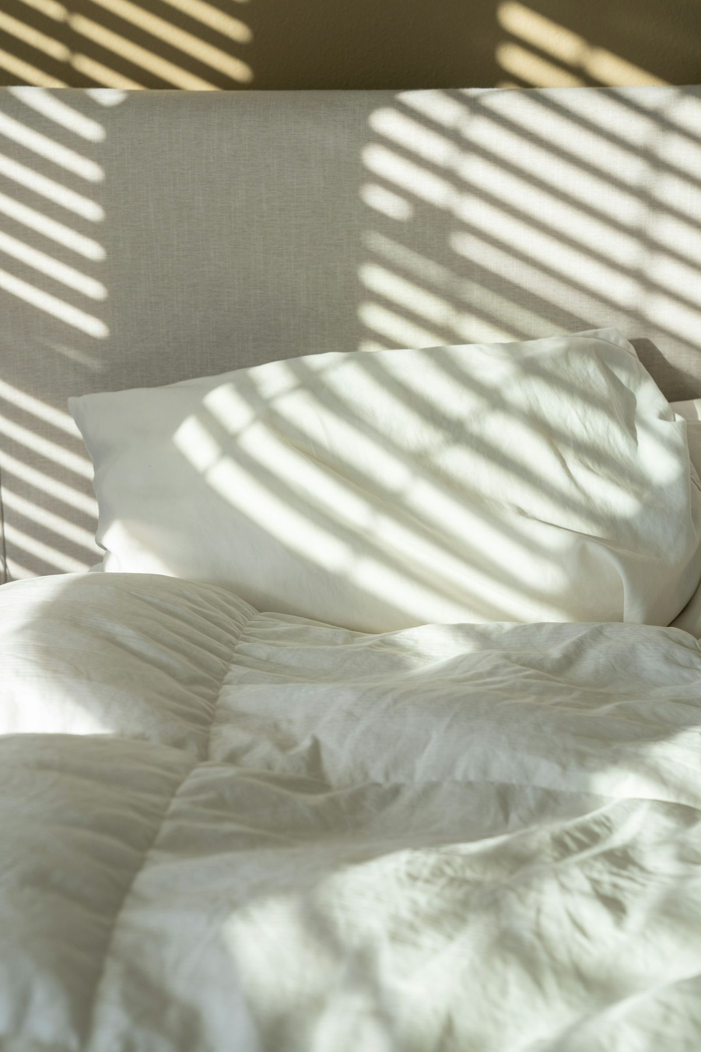 Stripes of morning light across a linen bed