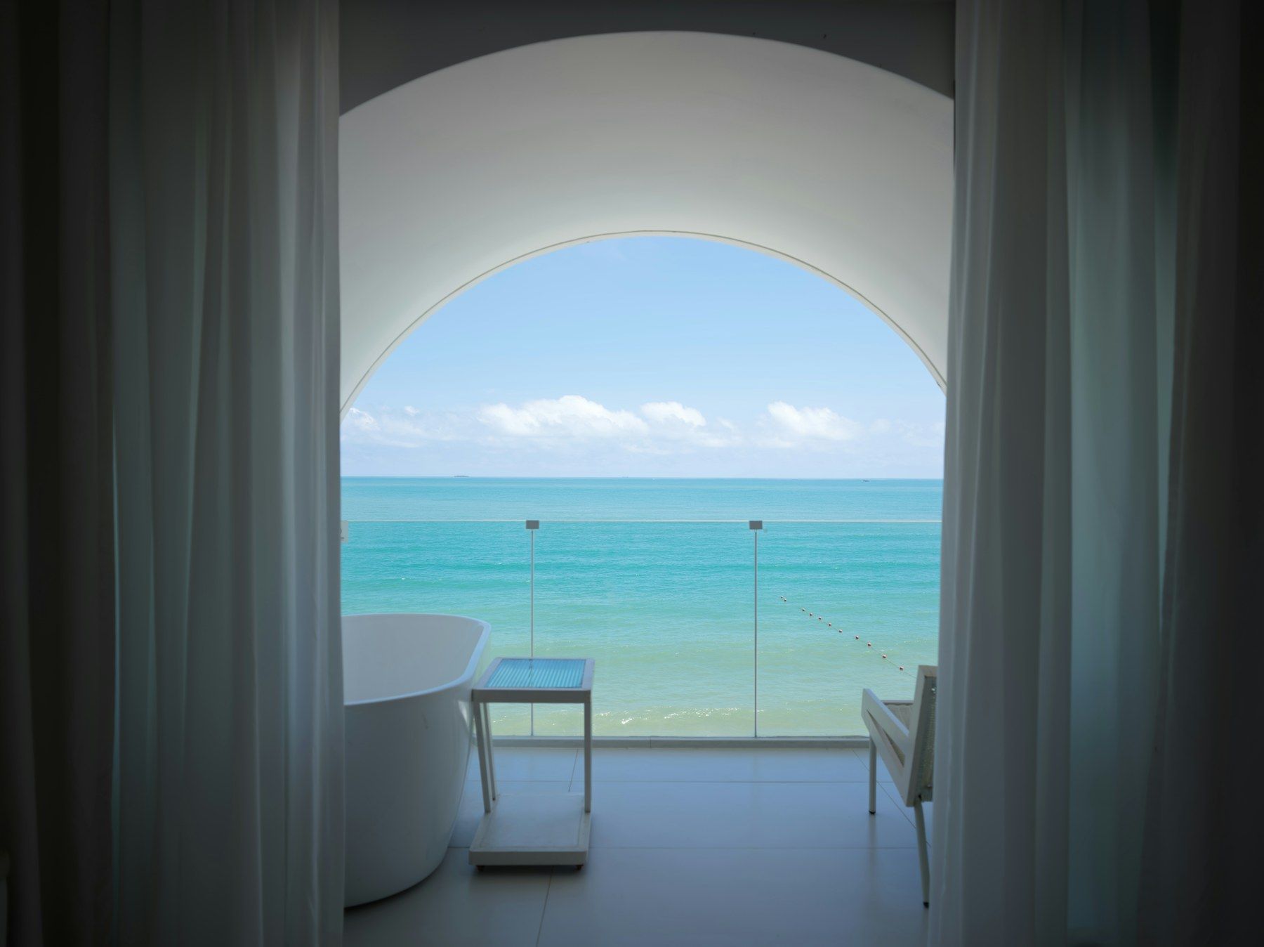 A white room with an arched window opening onto the sea