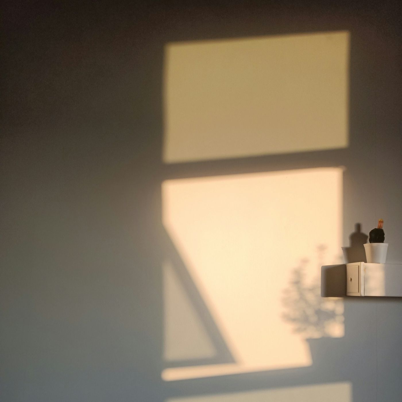A square of window light on a plaster wall beside a small shelf