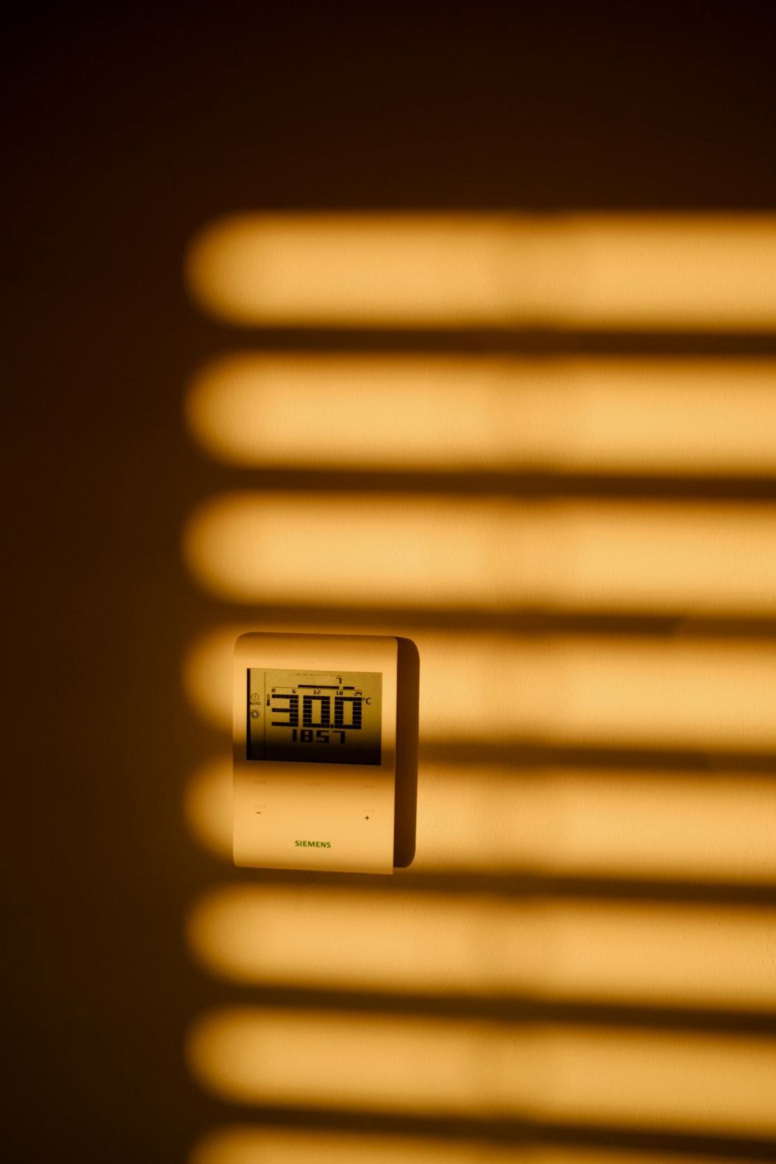 A room thermometer on a wall in warm striped sunlight